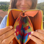 Person holding an open orange wallet with a colorful interior pocket.