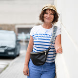Woman in a striped shirt and cap standing outdoors with a car in the background