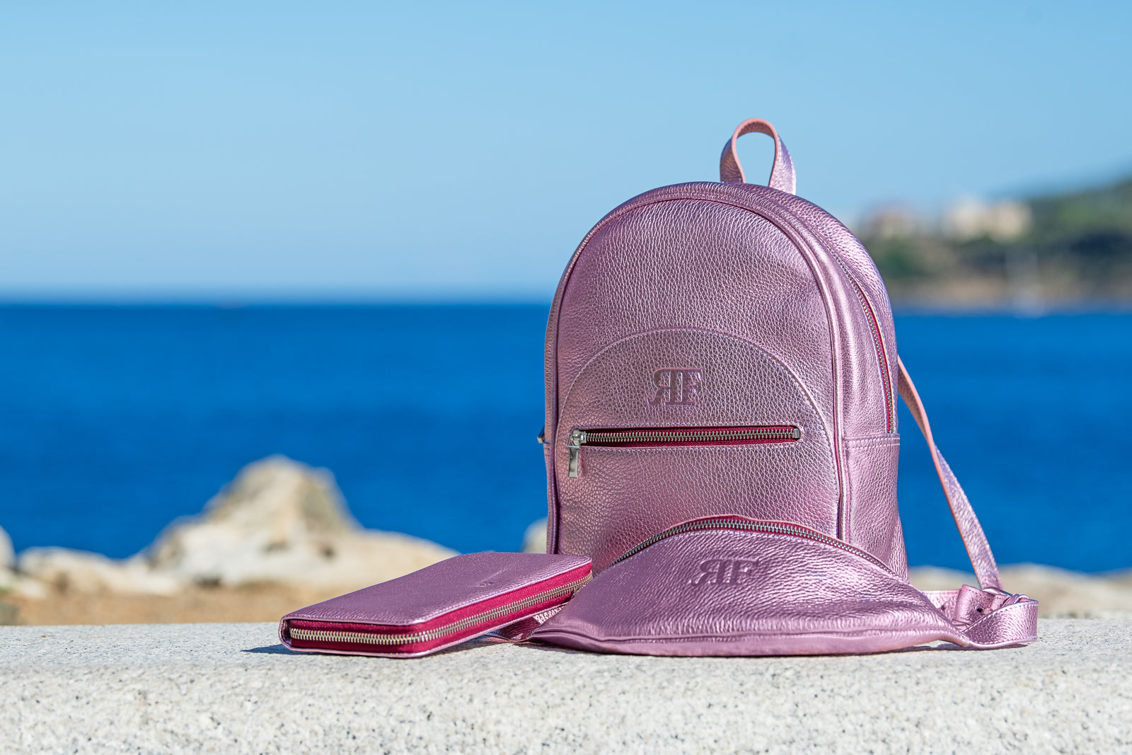 Pink backpack and wallet on a rock with ocean and sky background
