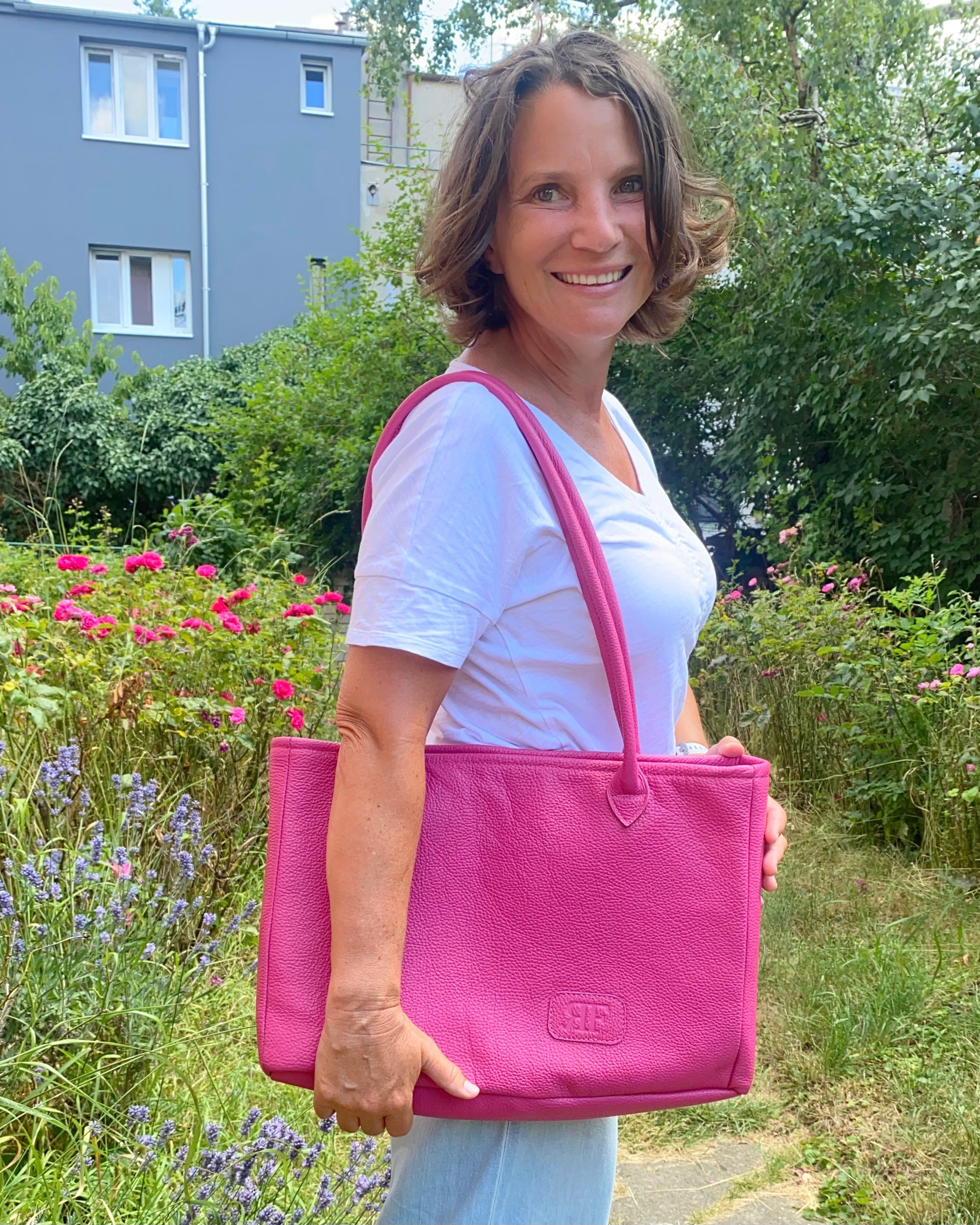 Woman holding a pink bag outdoors with greenery and flowers in the background
