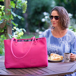 Woman sitting at a table outdoors with a pink bag and a cup of coffee.