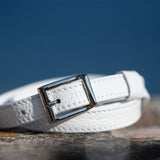White leather belt with a silver buckle on a stone surface with a blue sky background