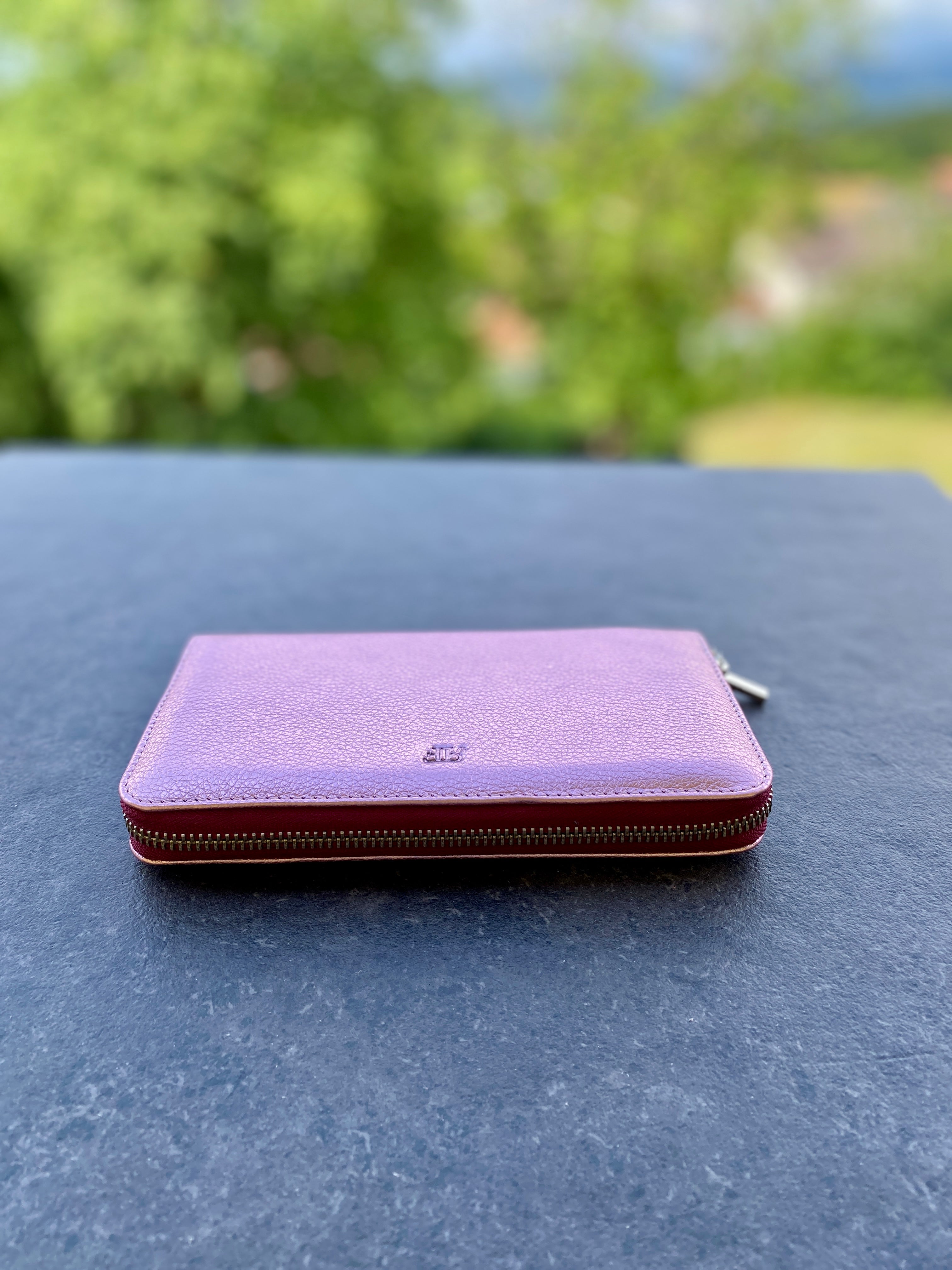 Purple wallet on a dark surface with a blurred green outdoor background