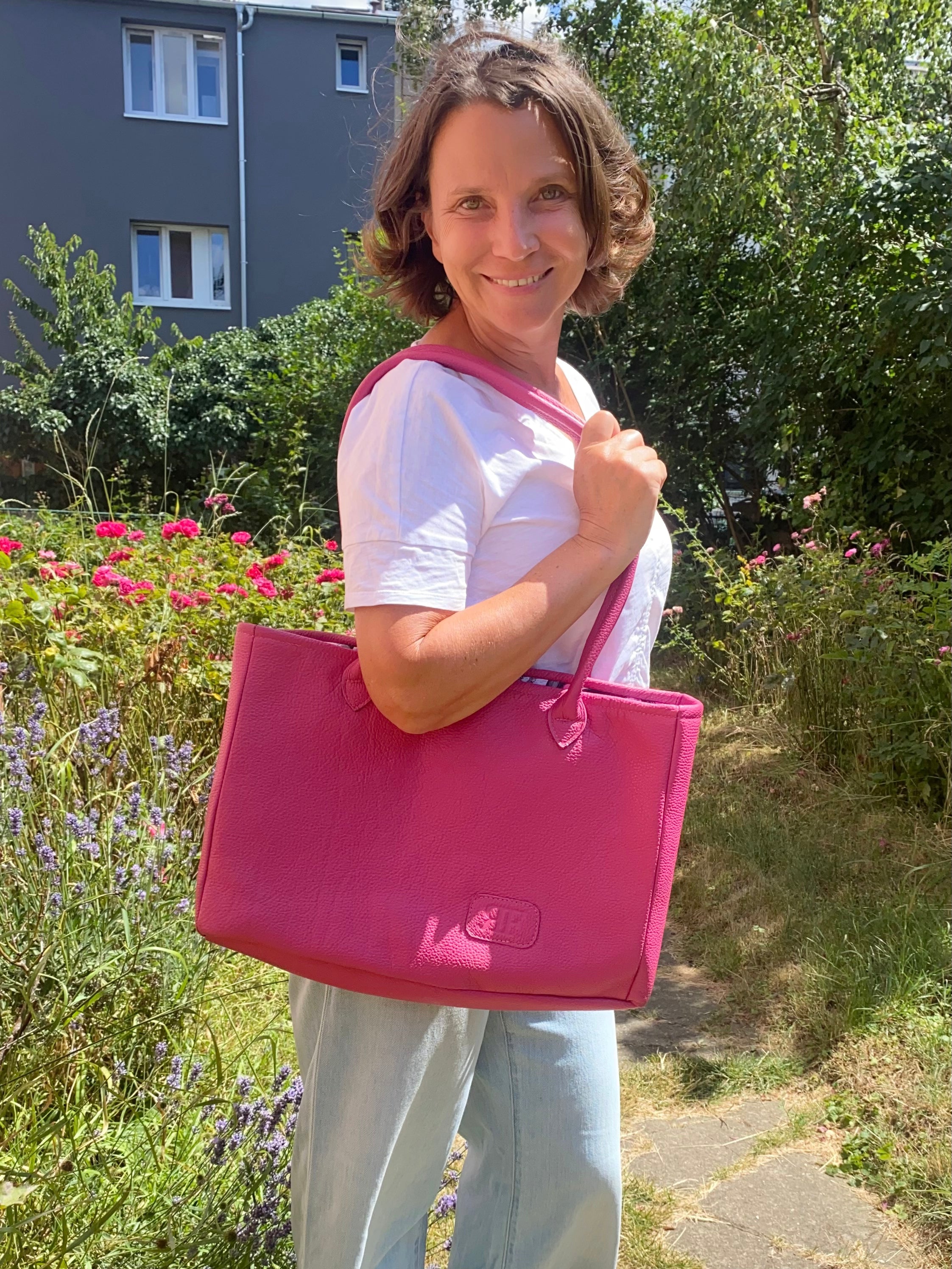 Woman holding a pink bag outdoors with greenery and flowers in the background