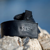 Black leather belt with a logo on a rock against a blurred natural background