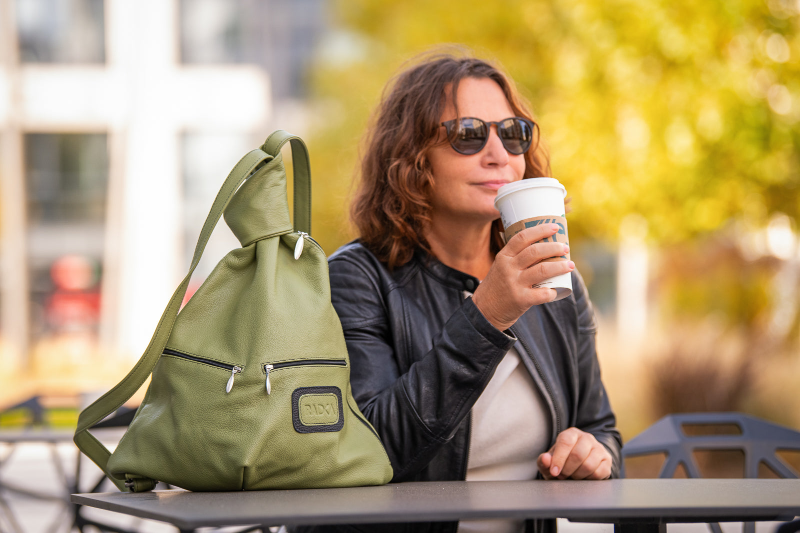 green leather backpack with a woman who drinks a coffee