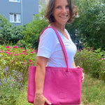 Woman holding a pink bag outdoors with greenery and flowers in the background