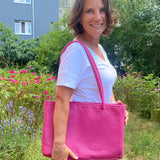 Woman holding a pink bag outdoors with greenery and flowers in the background