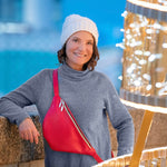 Woman wearing a gray sweater and white beanie with a red bag, standing in front of festive lights.