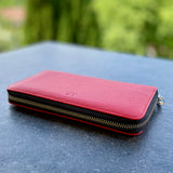 Pink wallet with gold zipper on a dark surface with a blurred green background