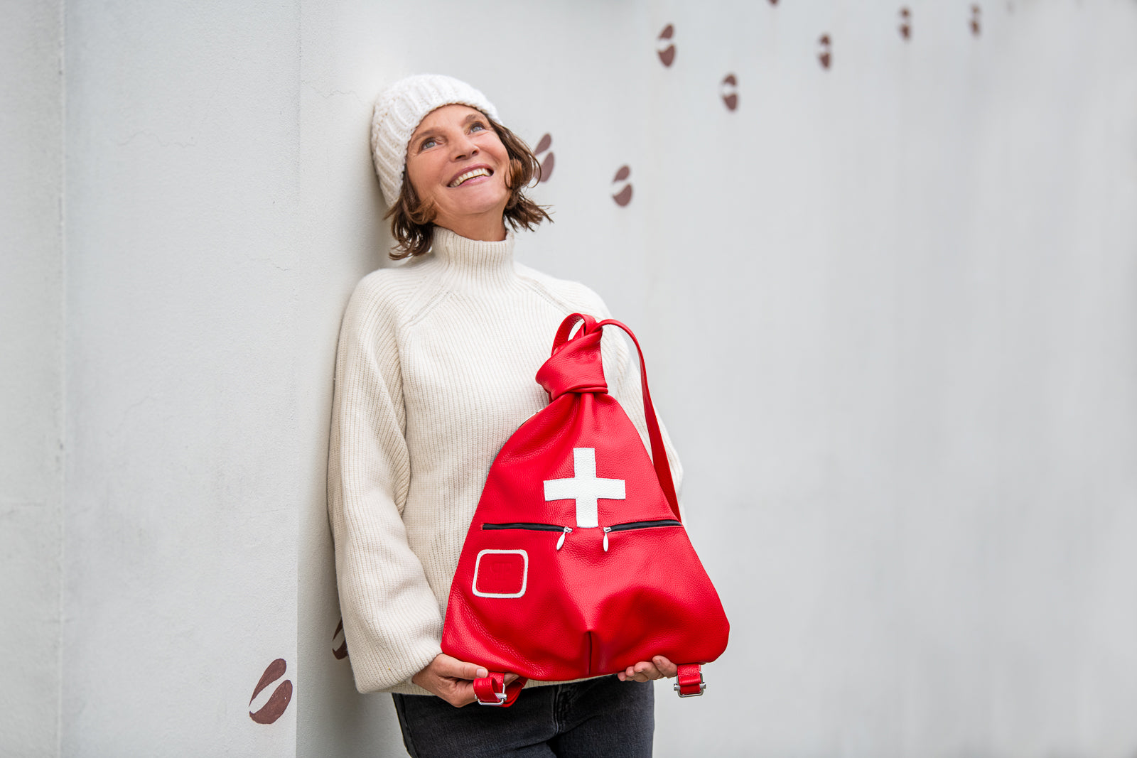Woman holding a red drawstring bag with a white cross against a light gray background