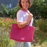 Woman holding a pink bag outdoors with greenery and flowers in the background