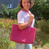 Woman holding a pink bag outdoors with greenery and flowers in the background